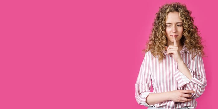 A young woman makes a gesture with her hands quietly, applying them to her lips. Isolated on pink background