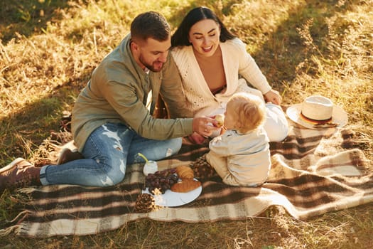 Illuminated by sunlight. Happy family of father, mother and little daughter is in the forest.