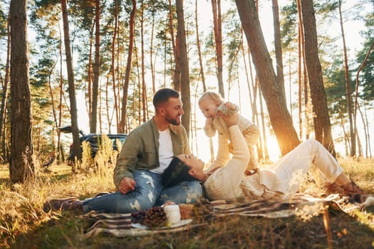 Illuminated by sunlight. Happy family of father, mother and little daughter is in the forest.