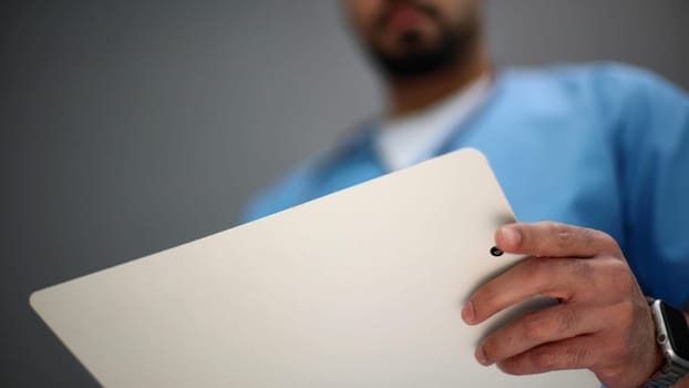 Portrait of a senior doctor holding notes against a gray background.