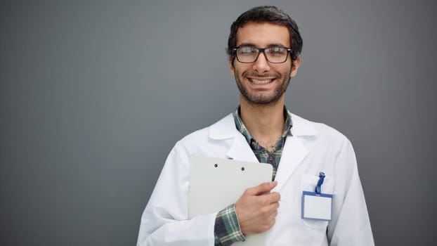 Portrait of positive male doctor posing and smiling at camera on gray studio background