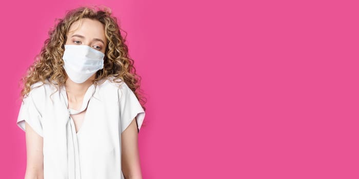 Young woman with a medical mask on her face shrugs. Isolated pink background