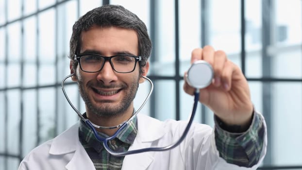Close-up portrait of doctor showing stethoscope on gray background