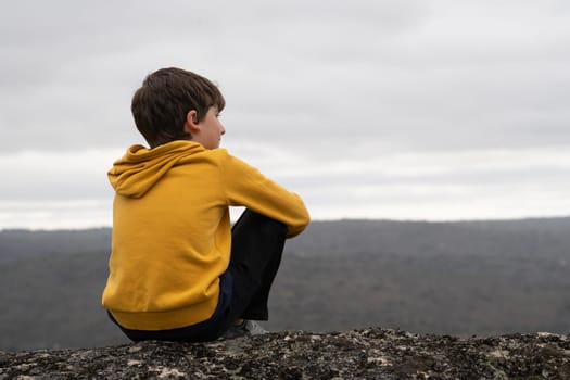 Calm Young boy sitting in the top of a mountain looking at the horizon with copy space.