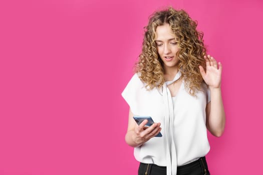 Young woman communicates through the phone by video link, expressing emotions. Female portrait. Isolated on pink background