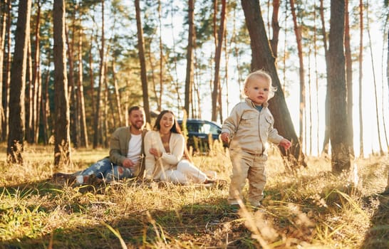 Little girl is running. Happy family of father, mother and little daughter is in the forest.