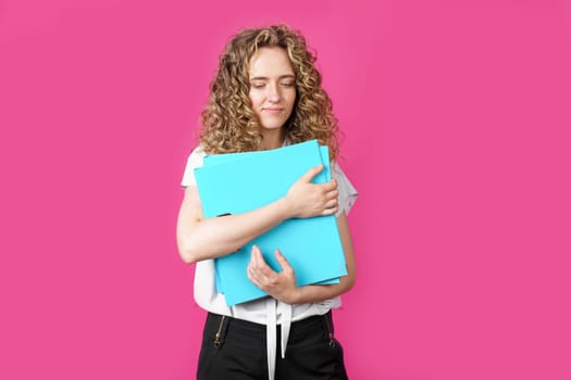 A young woman holds folders with documents in her hands. Isolated on pink background