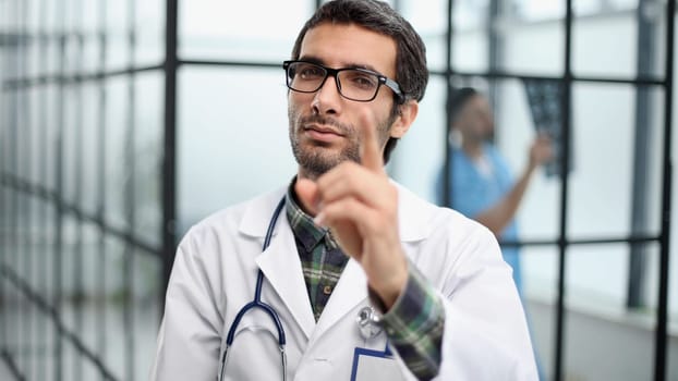 attentive doctor in a white coat pointing his finger at you while standing in the corridor of the hospital