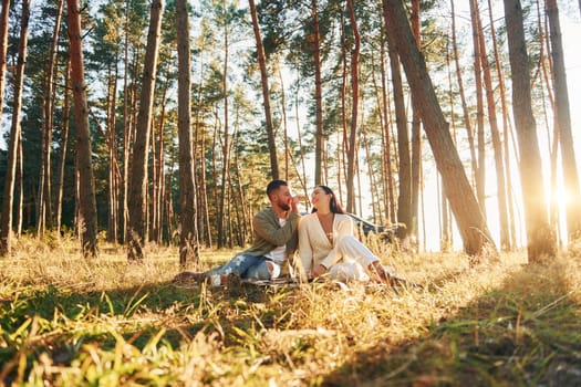 Happy couple sitting on the ground in the forest.