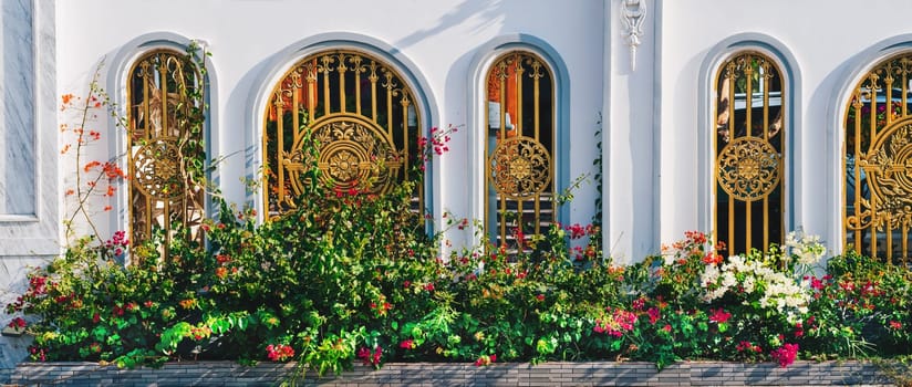 A white building with gold gate red yellow flowers background green luxury splendor.