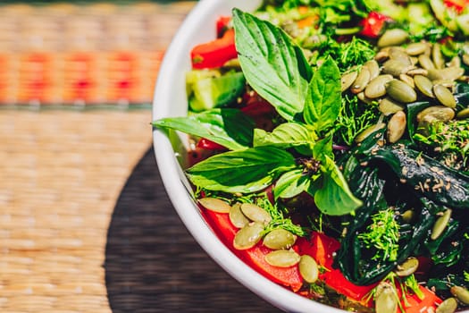A bowl of salad green seeds pumpkin basil leaves tomato juice seaweed.