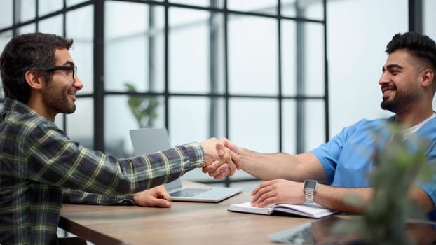 Cheerful male patient and doctor shaking hands.