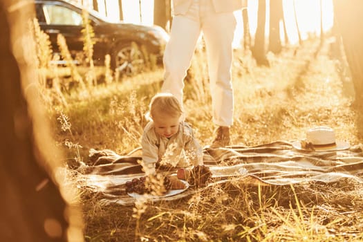 Little girl playing in the forest. Mother's legs is on the picture.
