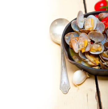 fresh clams stewed on an iron skillet over wite rustic wood table 