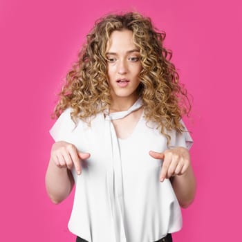 Charming woman with positive facial expression, showing thumbs down. Isolated on a pink background. Take a look, please