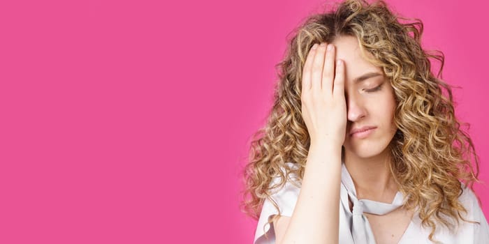 A young woman holds on to her sore head. Female portrait. Isolated on pink background