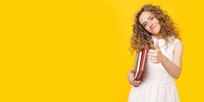 A young woman is holding a diary and a textbook. Shows gesture class. Female portrait. Isolated on yellow background