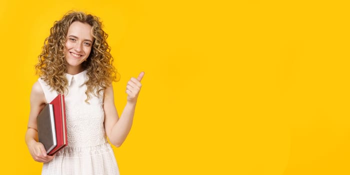 A young woman is holding a diary and a textbook. Shows gesture class. Female portrait. Isolated on yellow background