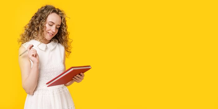 A young woman holds a textbook and a pen. Female portrait. Isolated on yellow background