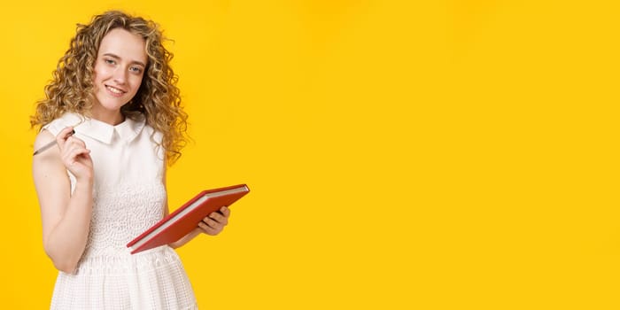 A young woman holds a textbook and a pen. Female portrait. Isolated on yellow background