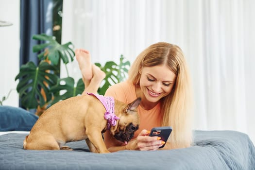 Laying down on bed. Woman with pug dog is at home at daytime.