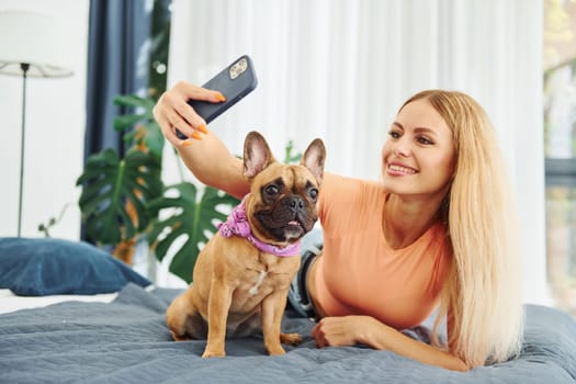 Doing selfie. Woman with pug dog is at home at daytime.