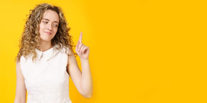 Portrait of a young smiling woman who raised her finger to the top. Female portrait. Isolated on yellow background