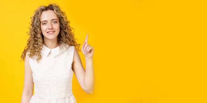 Portrait of a young smiling woman who raised her finger to the top. Female portrait. Isolated on yellow background