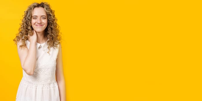 Portrait of a young smiling woman who holds her hand around her neck. Female portrait. Isolated on yellow background