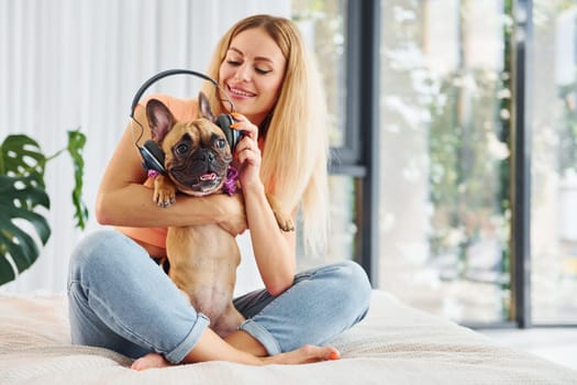Putting headphones on pet. Woman with pug dog is at home at daytime.