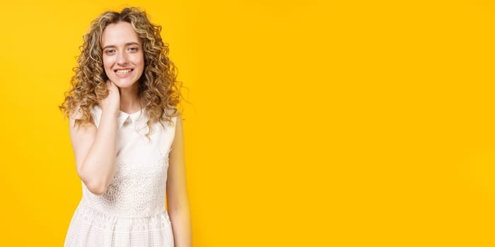 Portrait of a young smiling woman who holds her hand around her neck. Female portrait. Isolated on yellow background