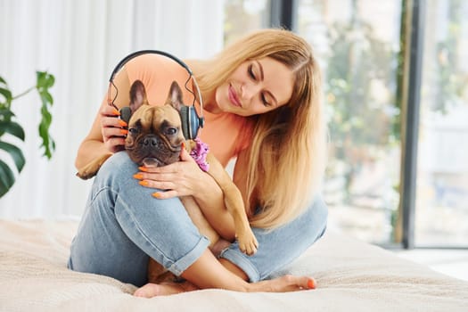 Putting headphones on pet. Woman with pug dog is at home at daytime.