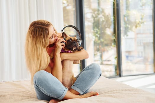Putting headphones on pet. Woman with pug dog is at home at daytime.