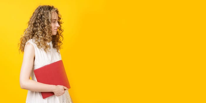 Portrait of a young smiling woman who holds a book in her hands. Female portrait. Isolated on yellow background