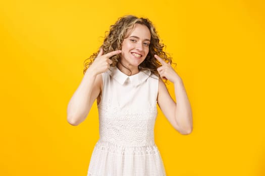 Portrait of a young smiling woman showing her smile with her fingers. Female portrait. Isolated on yellow background