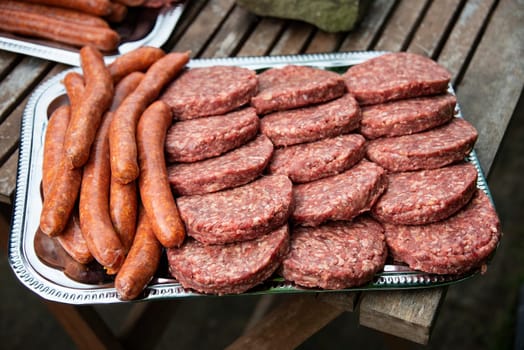 burgers and sausages on a payment place ready for the barbecue or to fry in a pan