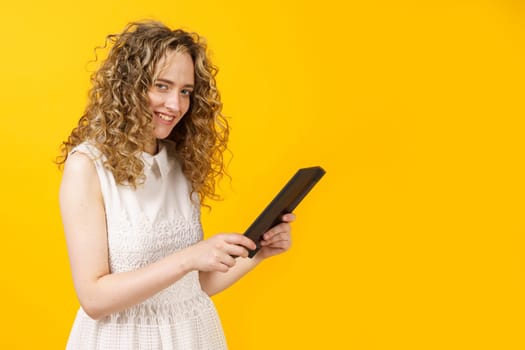 Portrait of a young woman who communicates on a tablet. Female portrait. Isolated on yellow background