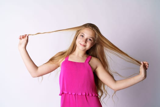 A cute and happy girl of Caucasian appearance in pink clothes on a white background plays with her long hair.