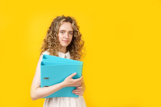 A young woman holds folders with documents in her hands. Isolated on yellow background