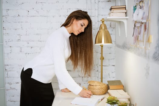 business woman in a white sweater writes in a notebook while sitting at the table