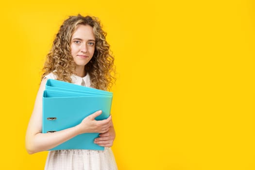 A young woman holds folders with documents in her hands. Isolated on yellow background