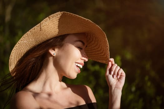 Cheerful young woman in straw sun hat smiles toothy smile close up on summer sunny day