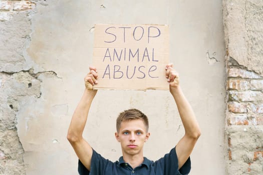 Young man holding the inscription stop animal abuse in his hands. Caucasian guy in protection of animals came out to protest. Animal rights conceptual image