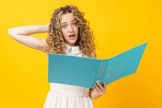 A young woman holds folders with documents in her hands. Reads and wonders. Isolated on yellow background