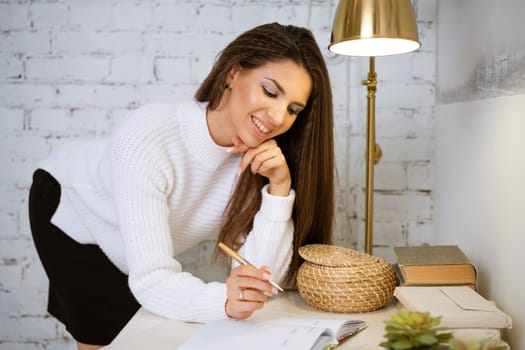 business woman in a white sweater writes in a notebook while sitting at the table