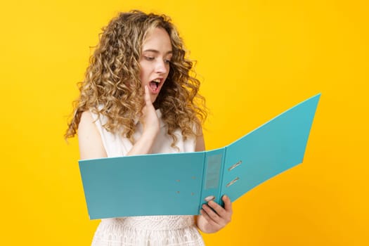 A young woman holds folders with documents in her hands. Reads and wonders. Isolated on yellow background