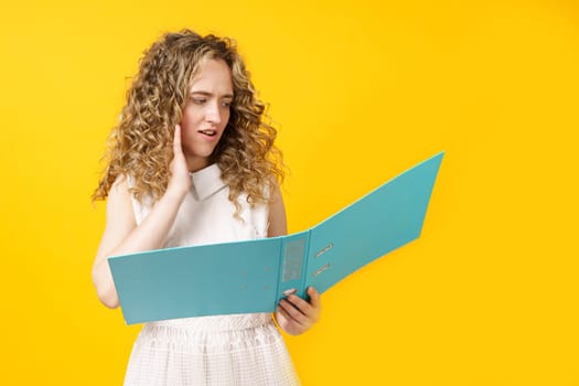 A young woman holds folders with documents in her hands. Reads and wonders. Isolated on yellow background