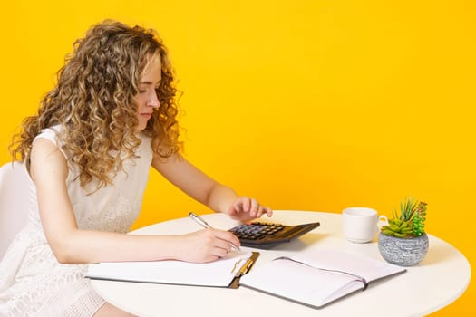 A young woman sits at a table, works with documents, considers, studies. Education. Business. Isolated on yellow background