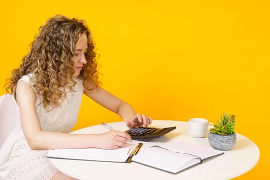 A young woman sits at a table, works with documents, considers, studies. Education. Business. Isolated on yellow background