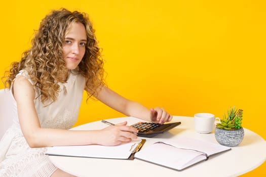 A young woman sits at a table, works with documents, considers, studies. Education. Business. Isolated on yellow background